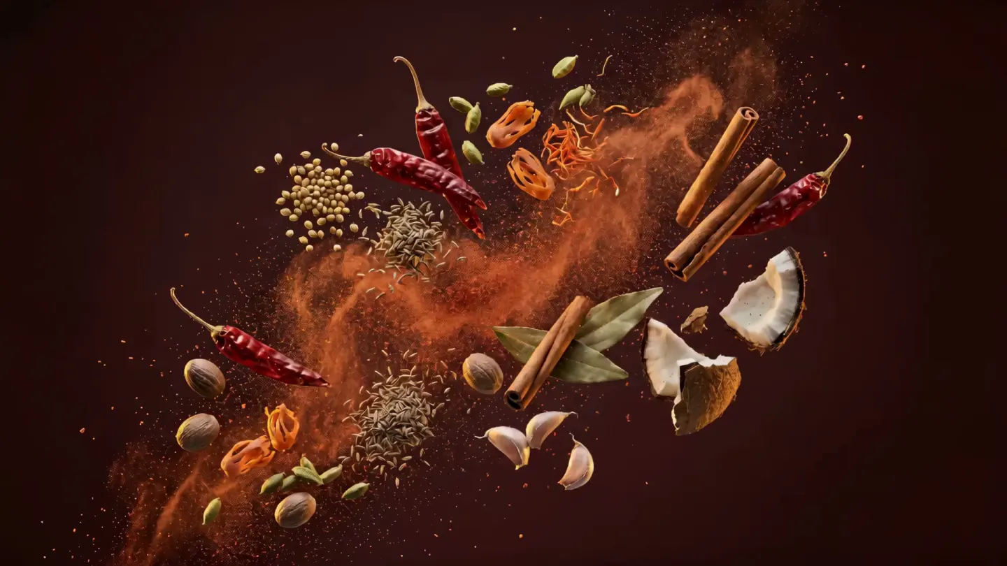 Whole spices for Kolhapuri masala scattered through a cloud of chilli powder